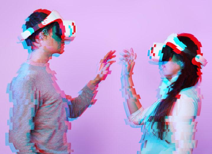 A man and woman facing each other, presented in a glitchy, vapourwave style effect against a light pink background. They are wearing VR headsets and they are both stretching their arms, bent at the elbows as though they are touching.