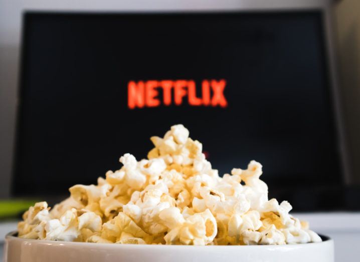 Stock image of a bowl of popcorn, in front of a TV with the Netflix logo displayed on the screen.