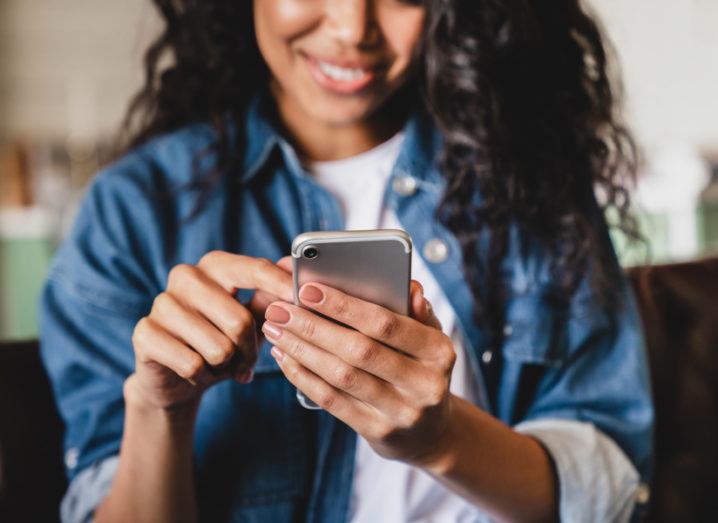 Cropped shot of a young woman smiling while using a smartphone.