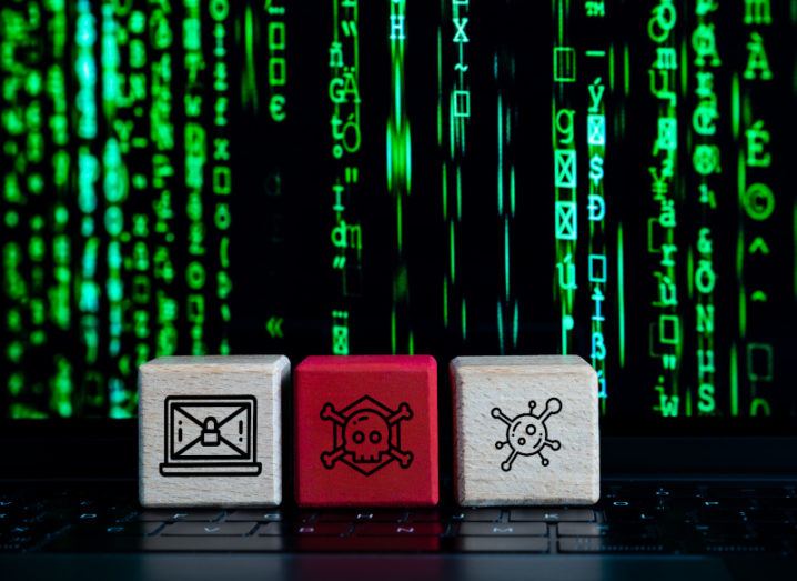 Three blocks, two white and one red, sit on a keyboard with various symbols showing a cyberattack against the backdrop of lines of green code.