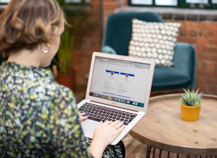 View over the shoulder of a young woman in a floral dress, to see she is accessing the Unibuddy platform on a laptop.