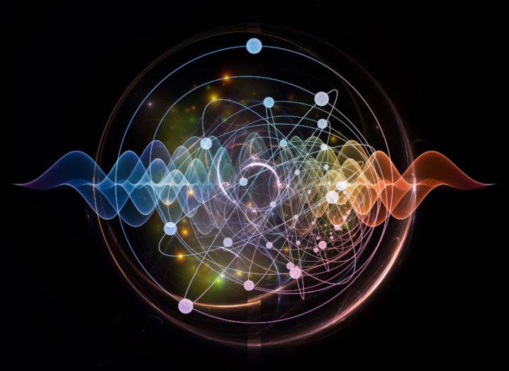 An artist’s depiction of an atom is shown. Electrons can be seen orbiting around the nucleus. The orbits are depicted by lines. The left-hand side of the picture is blue and gradually transitions into orange on the right.