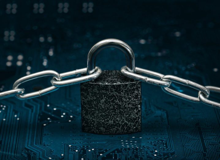 A locked padlock sits on a computer motherboard with two chains connected to either side of the lock, symbolising blockchain.