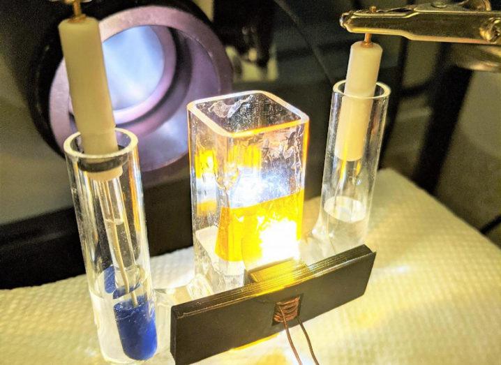 The team's experimental apparatus for splitting water is shown. There are two test tubes on either side of the central device with water in the tubes. There are electrodes in the water which are connected to the central element. The central element is glowing yellow.