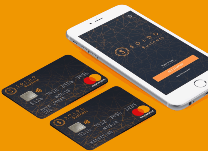 The Soldo app is open on a smartphone, with two payment cards sitting beside it.