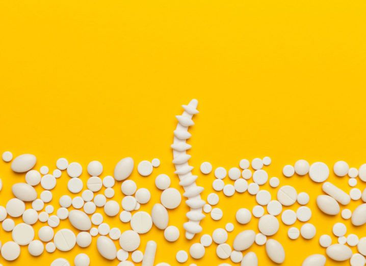 A spinal cord rests against a yellow background, surrounded by pills.