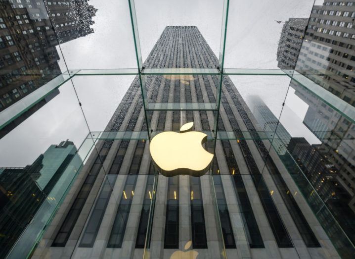 The Apple logo glows above the glass roof of a building on a rainy day.