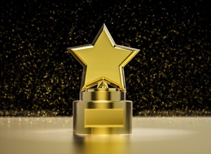 A gold trophy with a star on top of it sits against a black background.