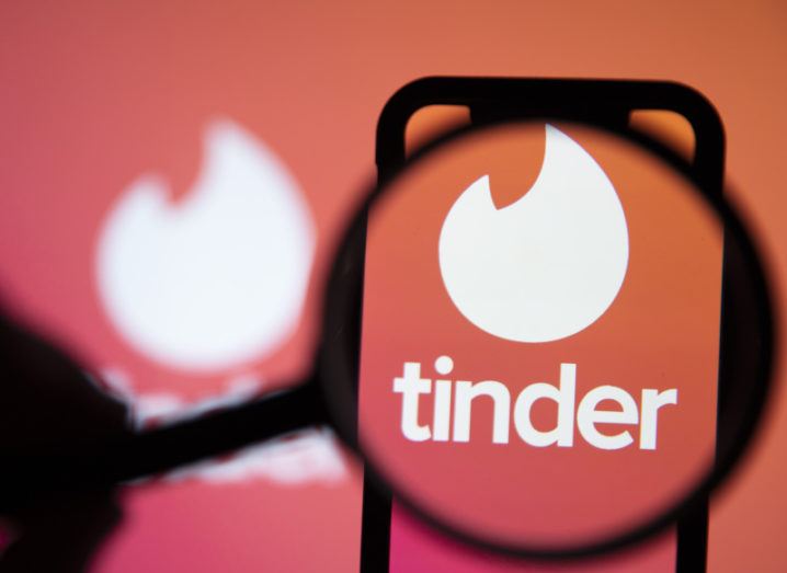 Tinder dating app logo displayed on a smartphone under a magnifying glass.