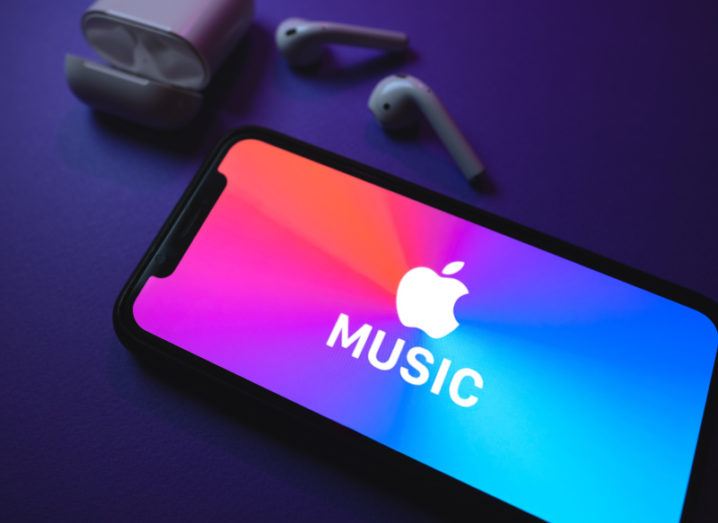 The Apple Music logo displayed on a smartphone screen. The phone is next to a pair of AirPods.