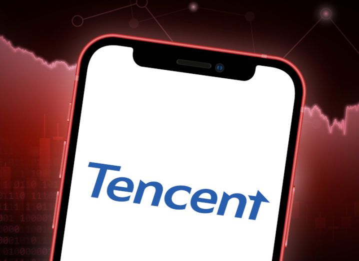 The Tencent logo on a phone screen in front of a stock price graphic.