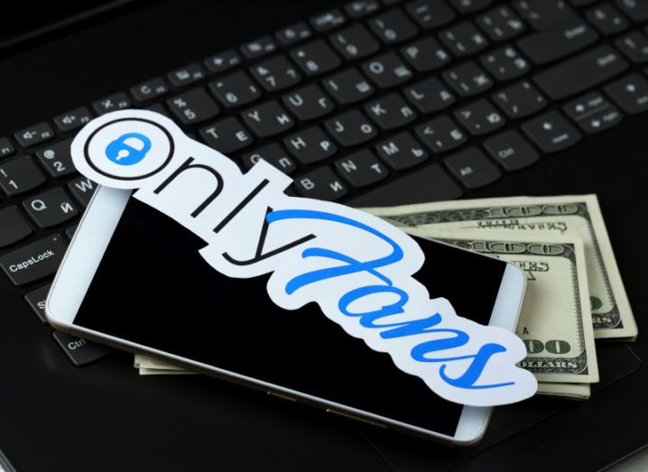 The OnlyFans logo sitting on top of a mobile phone and a pile of banknotes.
