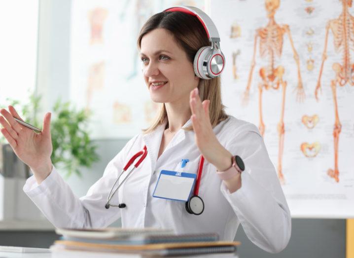 Scientist/doctor doing a remote consultation or lesson in a classroom surrounded by anatomy posters and wearing a stethoscope indicating she is a doctor or medical professional.