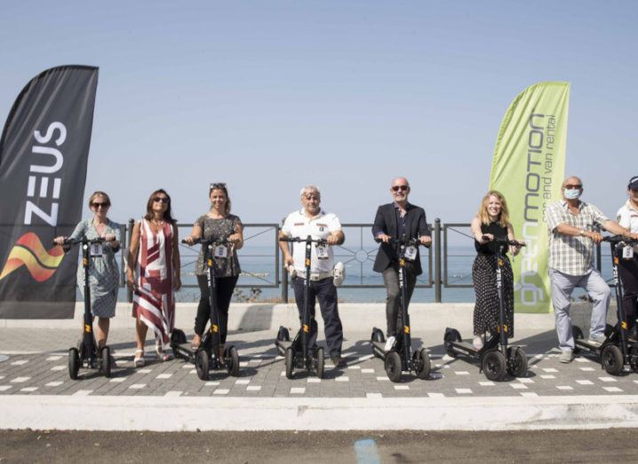 Teams from e-scooter company Zeus and Green Motion are pictured at Zeus's Italian launch in the coastal town of Anzio, with a blue sky in the background.