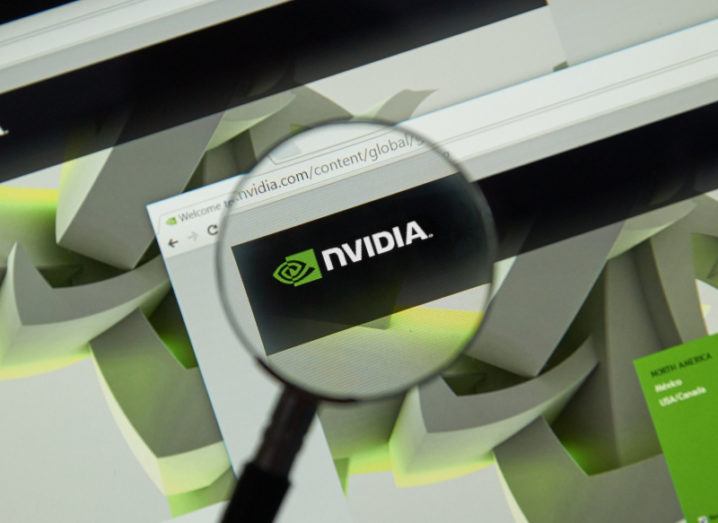 The Nvidia website is on a computer monitor and someone is looking at the Nvidia site through a magnifying glass. The Nvidia logo is in the centre of the magnifying glass.