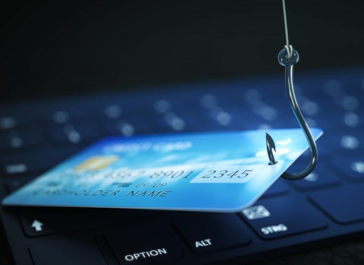 Laptop with a credit card resting on its keyboard. A fish hook is piercing the credit card to make it look like a phishing scam concept.