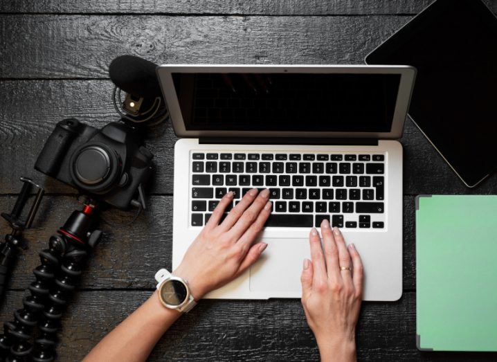 A person is working at a laptop with a camera on the table beside them.