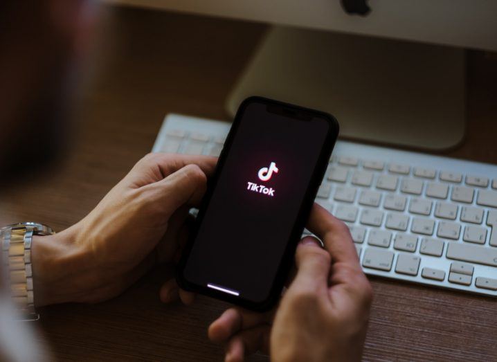 View over a person's shoulder as they use their phone, with the TikTok logo visible on the phone screen.