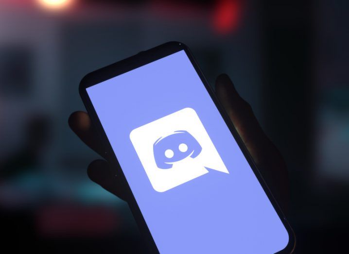 A smartphone displaying the logo of Discord, which is a white speech bubble on a lavender background, containing a videogame controller icon stylised to look like a face.