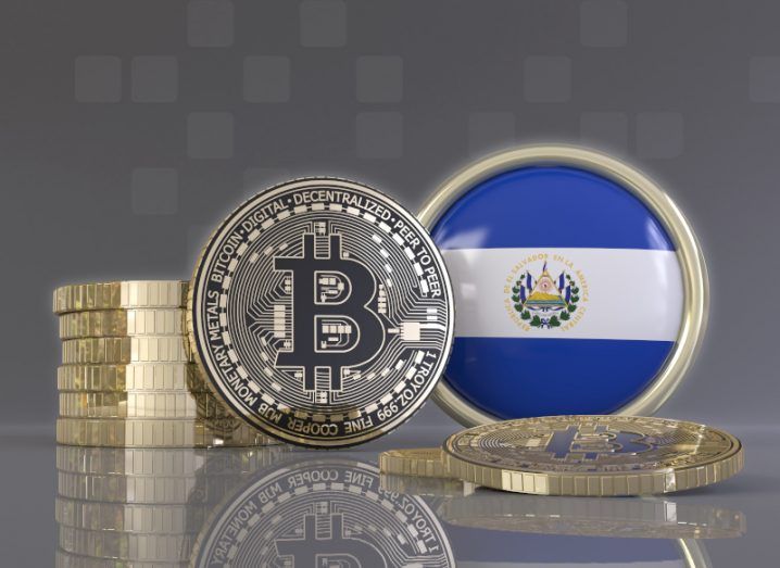 Illustration of gold coins bearing the bitcoin currency symbol stacked next to a badge bearing the El Salvador flag.