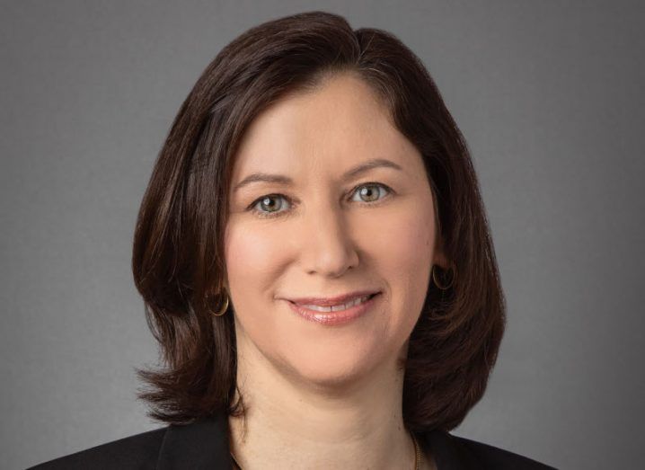 A headshot of a woman with brown hair smiling at the camera against a grey background. She is the CIO of IBM.