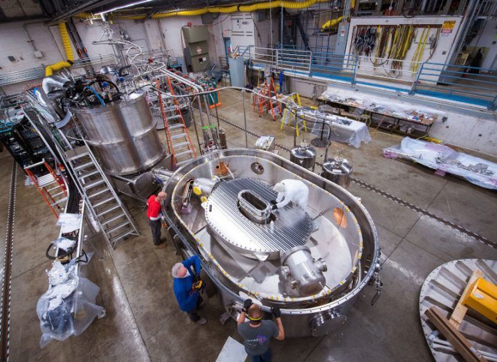The team can be seen working on the magnet at the test stand at MIT. There are four people working on the donut-shaped device that is intended to help generate fusion energy.