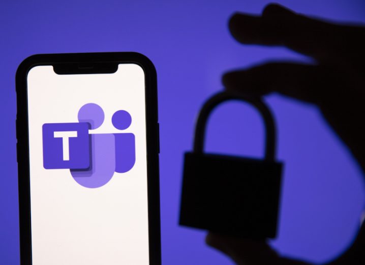 Microsoft Teams logo on a smartphone with a silhouette of a hand holding a lock against a purple background.