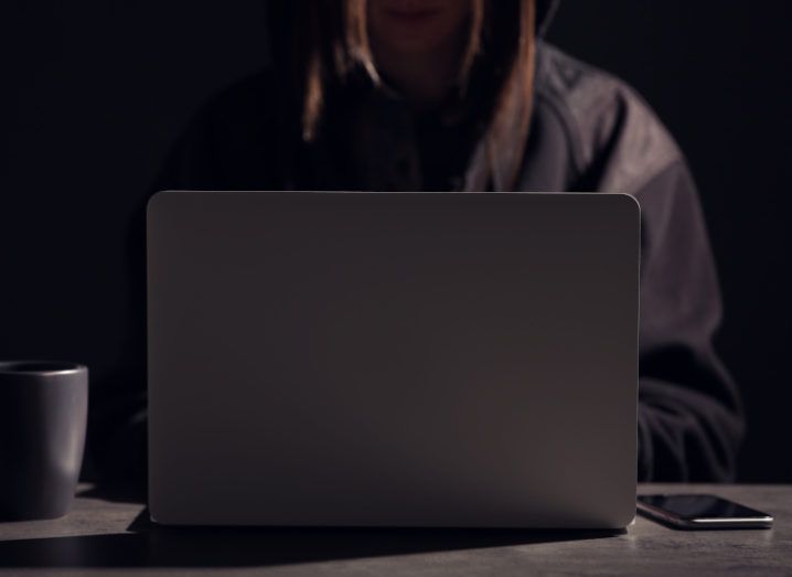 A woman in a dark room working on a laptop.