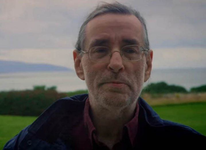 Headshot of professor Dave Reid smiling with hilly landscape in the background.