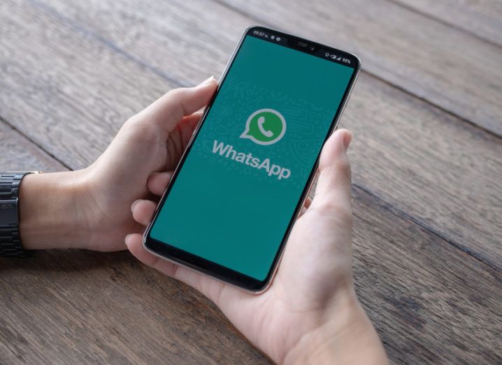 A person is holding a smartphone with the WhatsApp logo on the screen.
