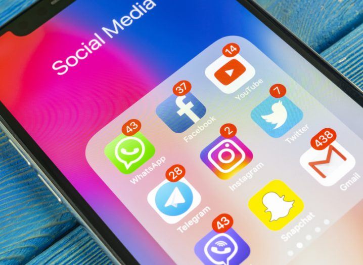 A phone is sitting on a table with a number of social media apps visible on the home screen, including Facebook, Twitter, Snapchat, and Google apps Gmail and YouTube.