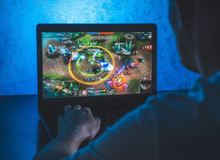 A look over the shoulder of a person playing League of Legends on a PC laptop in a darkened room.