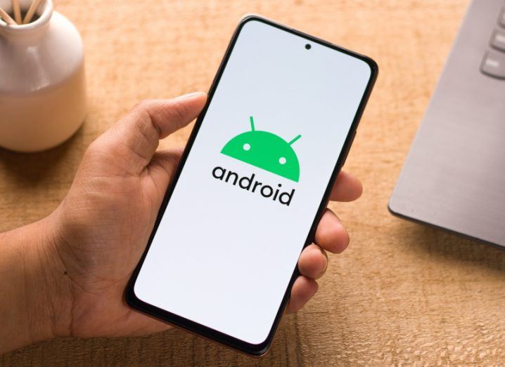 Person's hand holding a phone with the Android logo on its screen.