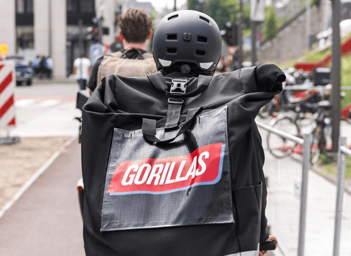 A bag with the Gorillas logo on it can be seen on the back of a person riding a bike through a city street.