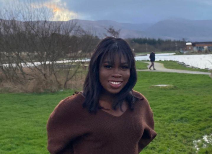 Genetics researchers Ifeolutembi Fashina pictured out in a park with mountains visible in the distance. She is wearing a brown jumper.
