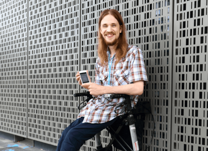 Access Earth CEO Matthew McCann seated on an accessibility chair with a smartphone in his hand displaying the Access Earth app.