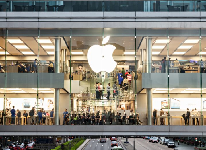 Apple store in Hong Kong. Apple logo placed on a glass front wall with people walking around inside the building.