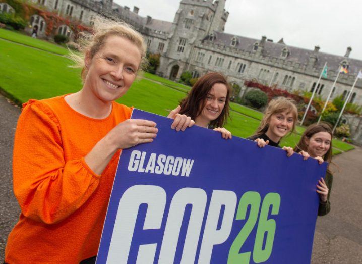 Four women delegates standing in a row on the UCC campus holding a blue banner that reads "Glasgow COP26".