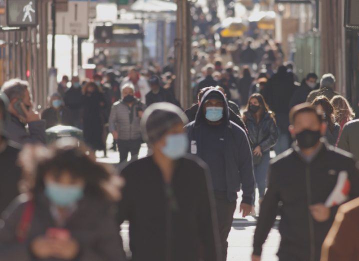 Crowd of people walking on a street wearing masks.