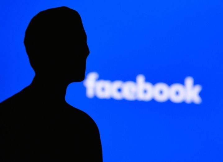 Silhouette in the shape of Mark Zuckerberg with the Facebook logo behind him on a blue background.