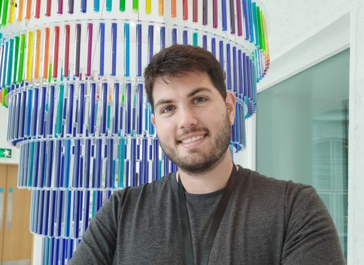 Fernando Garrido Diaz poses for a photograph in front of a large chandelier featuring glass tubes in a rainbow of colours.