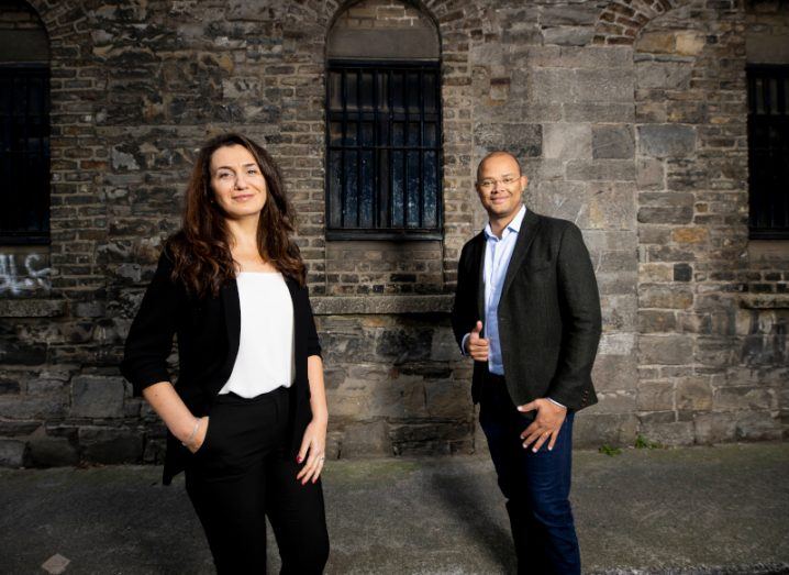 Kianda co-founders Darya and Osvaldo Sousa standing next to each other in business formals with brick wall and windows in the background.