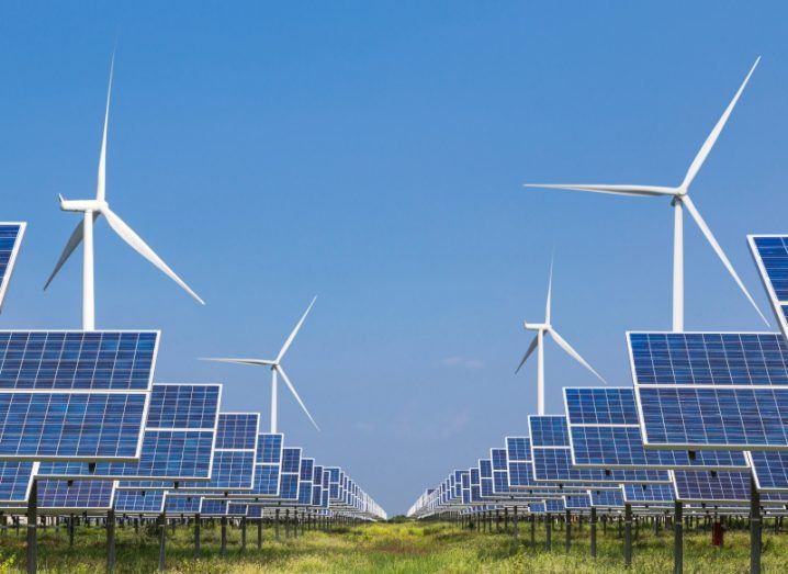 Solar panels and wind turbines on a field beneath a bright blue sky.