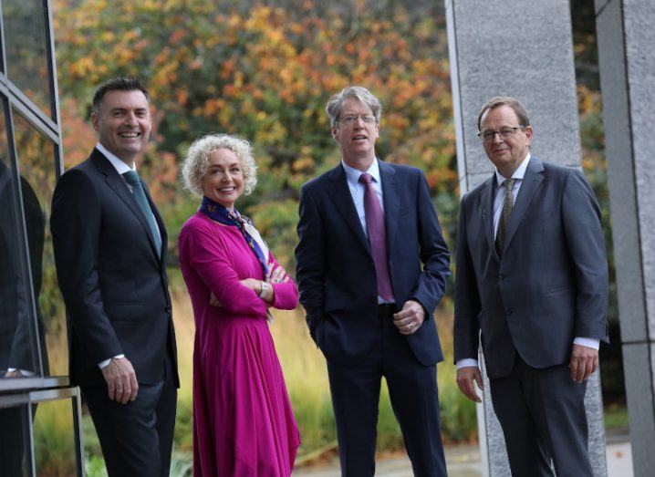 Siro CEO John Keaney, Vodafone CEO Anne O’Leary, ESB CEO Paddy Hayes, and VP of the European Investment Bank, Christian Kettel Thomsen, standing in a line and smiling at the camera. A glass building and trees are in the background.