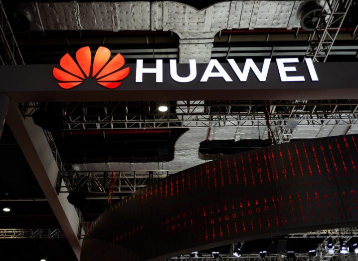 The Huawei logo is suspended from a roof in a large, dark room.
