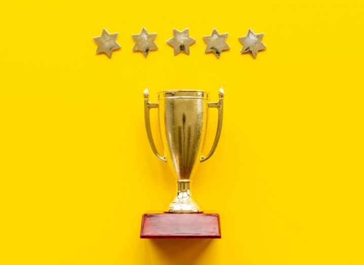 Gold trophy on bright yellow background with five gold stars in a row above it.