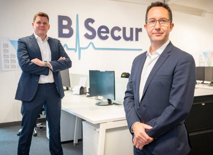 B-Secur's leadership team of two men standing a small distance apart in an office with the company logo on the wall behind them.