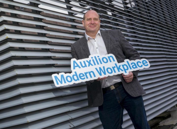A man stands holding a sign that says 'auxilion modern workplace'.
