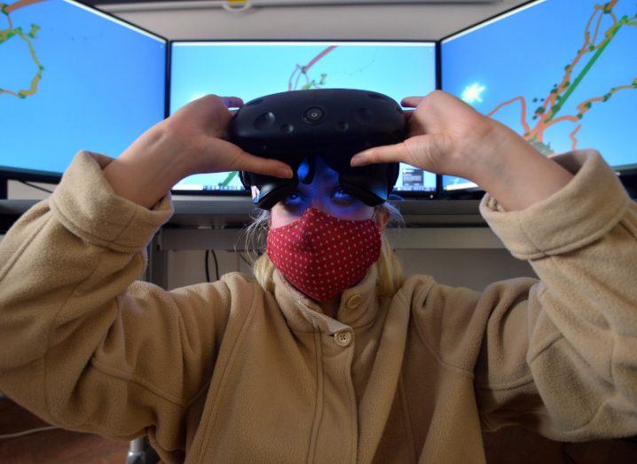 A woman using a VR headset with three giant screens in the background.