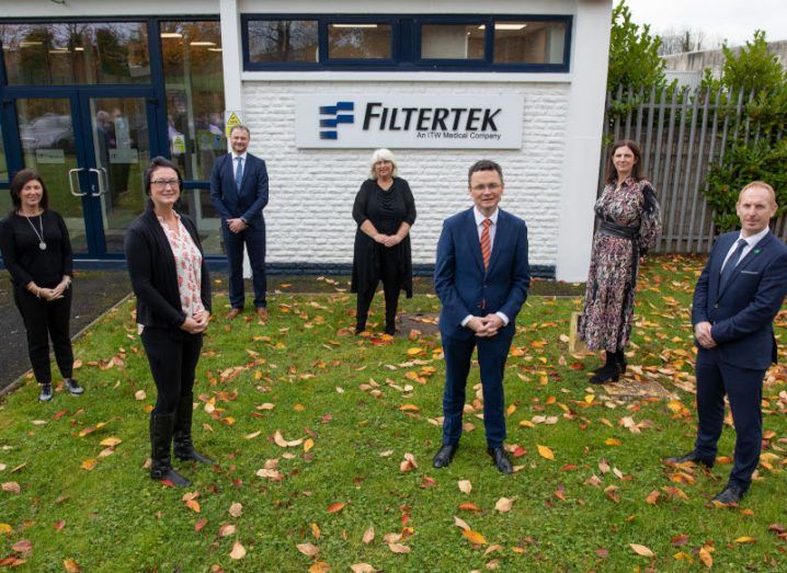 Seven people standing outside the Filtertek Limerick facility on a patch of grass strewn with leaves.
